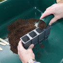 A person filling the grey propagator cells with soil.