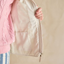 Close-up of the inside of a cream quilted waistcoat, showing the light lining and an internal pocket next to the zip.