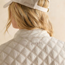 Close-up of the back of a cream quilted waistcoat, highlighting the diamond stitching and subtle Joules logo beneath the collar.