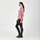 A person in equestrian attire with a pink polo, black riding breeches, and tall boots on a white background.