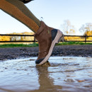 A close-up of a brown boot stepping into a muddy puddle, creating a splash.
