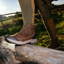 Person wearing brown boots stepping on a wooden log outdoors.