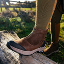 Person in brown boots standing on a log, outdoor setting with sun flare.