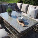 A stylish outdoor seating area featuring a wicker coffee table, cushions, and decorative items like a plant and glassware under sunlight.