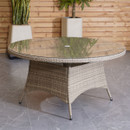 A round glass-top wicker patio table on a gray tile floor, with potted plants and a wooden slat wall in the background, creating a cosy outdoor vibe.