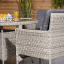 Outdoor seating scene featuring gray wicker chairs with dark cushions and a matching table. On the table are orange juice, flowers, and oranges.