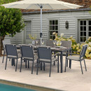 A stylish outdoor dining set with grey chairs and a table shaded by a large parasol, surrounded by blooming flowers and a pool.