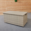 A beige wicker storage box with a flat lid, placed on a grey carpet in front of a light wooden panel wall. A small green plant decorates the wall.