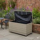 Rattan outdoor storage box with lid open, showing waterproof lining inside, placed on a patio beside a garden bed