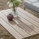 A light wooden teak table, featuring a glass vase of white roses and a small round clay vase.
