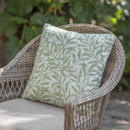 A close-up of a decorative green leaf-patterned cushion on a wicker chair, surrounded by lush greenery.