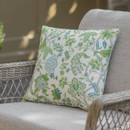 A decorative cushion with vibrant green and blue floral patterns rests on a light-coloured wicker chair, illuminated by soft sunlight.