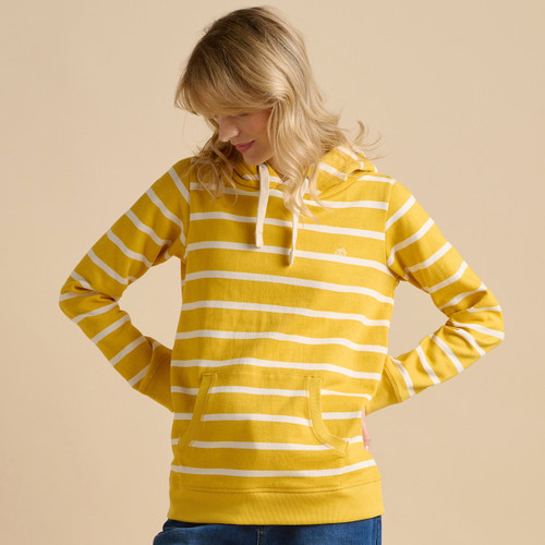 A person stands confidently in a yellow and white striped hoodie, hands on hips, against a soft beige background.