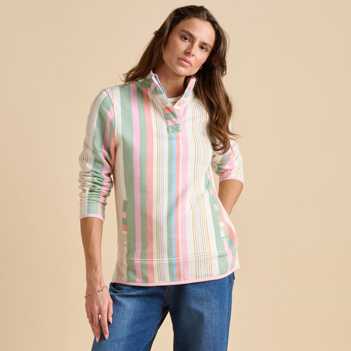 A woman poses in a multicoloured striped pullover, paired with blue jeans, against a neutral beige background.