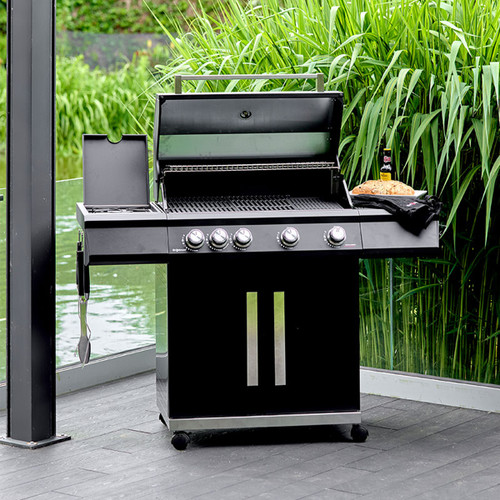 Black four-burner barbecue with the hood open, side shelves and double-door cupboard, shown on a patio by a lake.