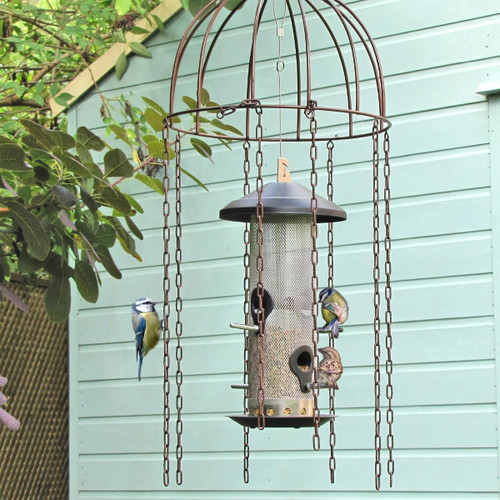 A cylindrical bird feeder covered by the metal bird feeder defender as it hangs from a tree.