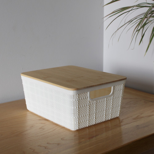 A white storage box with a woven effect and a bamboo lid positioned on a table.