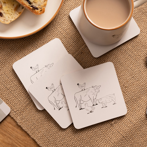 A view of a pack of 4 animal design cork Woodbury Lane coasters on a table next to a cup of tea