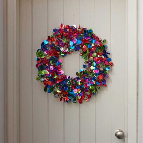 A vibrant, multicoloured decorative wreath made of shiny, overlapping discs hangs on a white wooden door.