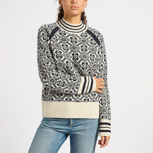 A person wearing a patterned navy and cream sweater with ribbed cuffs and a mock neck, paired with blue jeans.