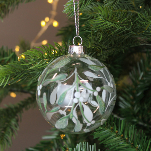 A view of a clear glass bauble with a glittery mistletoe design hanging on a Christmas tree