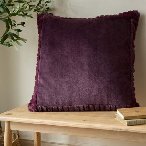 A view of a purple Catherine Lansfield velvet cushion on a wooden bench