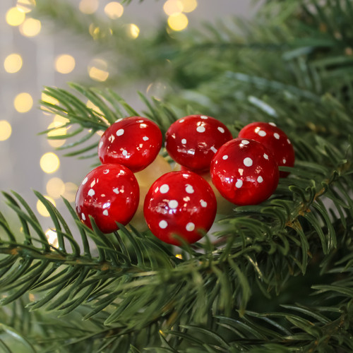 Red and white spotted mushroom ornaments on green pine branches, with soft golden bokeh lights in the background, evoke a festive, whimsical mood.