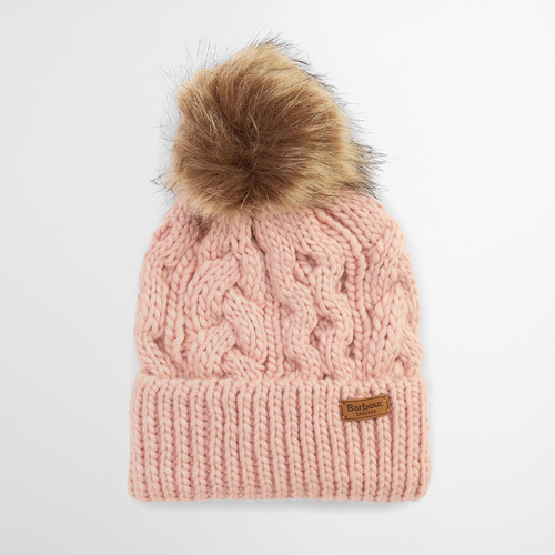 A pink knit beanie with a large brown faux fur pom-pom on top. It features a textured, cable-knit pattern and a leather tag on the folded brim.
