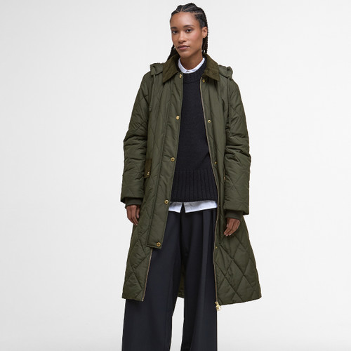 A person wearing a long, quilted olive-green coat with a black sweater and wide-leg pants. The setting is minimal, evoking a calm, stylish tone.