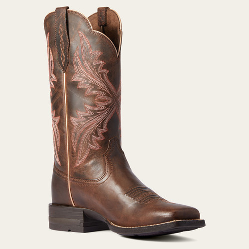 Brown leather western boot with intricate pink embroidery on the shaft, featuring a low heel and pull tabs. The tone is rustic and stylish.