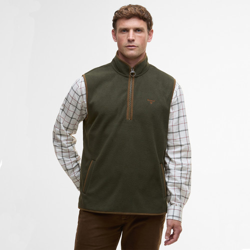 A man wearing a green fleece vest over a plaid shirt, standing against a plain white background. He appears calm and focused, exuding a casual style.