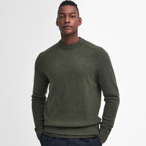 Man wearing a dark green sweater with ribbed cuffs and hem, standing against a plain white background. He looks relaxed and confident. Casual fashion.