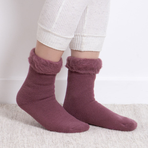 Pair of deep plum Totes bed socks with fluffy turn-down cuffs, worn with cream loungewear on a soft carpeted floor. Pair of deep plum Totes bed socks with fluffy turn-down cuffs, worn with cream loungewear on a soft carpeted floor.