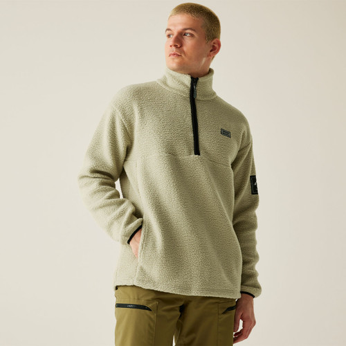A man wearing the beige fleece pullover with one hand in his pocket, standing at an angle and looking into the distance. The fleece features subtle logo detailing and a cozy high-neck collar.