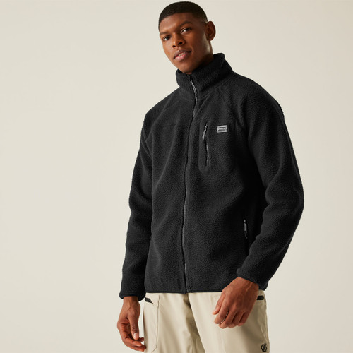 A man facing slightly left wearing the zipped black fleece jacket with beige outdoor trousers, styled for an outdoors-ready or athleisure look.