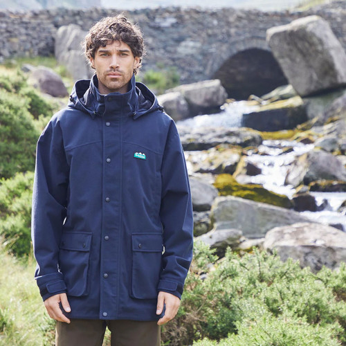 Man wearing a navy waterproof soft-shell jacket beside a rocky stream.