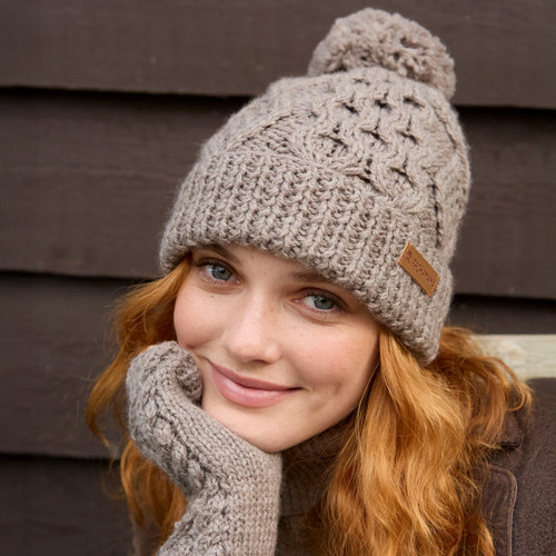 A woman wearing a cosy knitted hat and matching gloves, smiling in a winter setting.