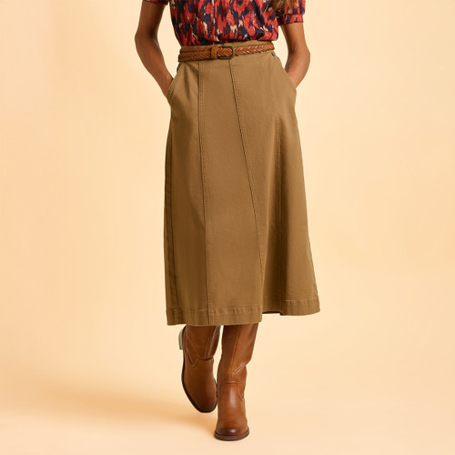 A person wearing a red patterned blouse and brown A-line skirt stands against a beige background, hands in pockets. Brown leather boots complete the outfit.