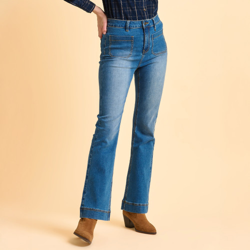 Person wearing high-waisted blue jeans with front pockets and a dark plaid shirt, styled with tan ankle boots. Background is a warm beige tone.