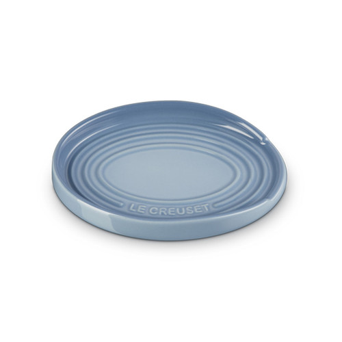 Le Creuset stoneware spoon rest in light blue, oval shape with raised edges and embossed branding, viewed from an angle.