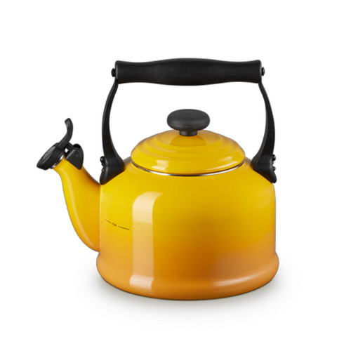 Angled front view of a Le Creuset enamel-on-steel whistling kettle in nectar yellow with a black handle and spout lever.
