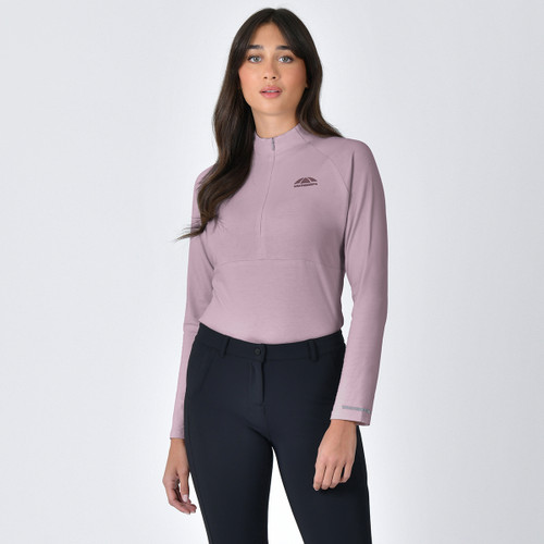 A woman stands against a plain background, wearing a light purple zip-up long-sleeve top and black leggings. Her expression is neutral and confident.