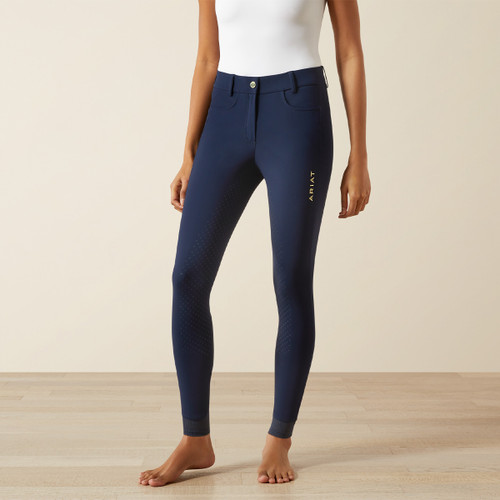 A person in a sleeveless white top and slim-fit, navy riding pants stands barefoot on a light wood floor, conveying a casual and elegant style.