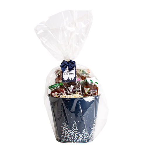Gift basket with cheese, crackers, and snacks, wrapped in clear plastic with a blue ribbon. The navy container has white trees, evoking a festive feel.
