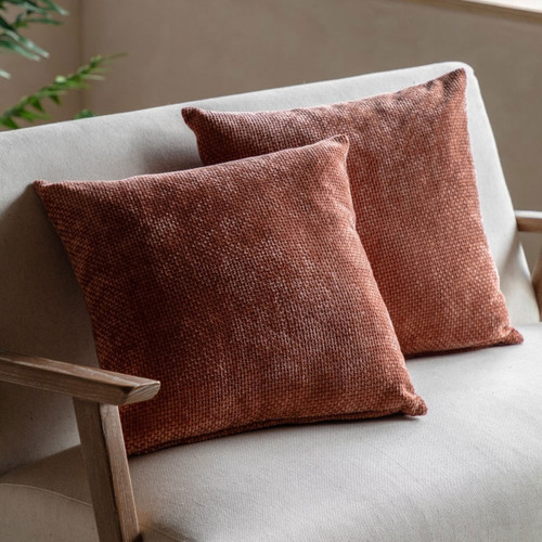 Two textured rust-coloured cushions on a neutral sofa.