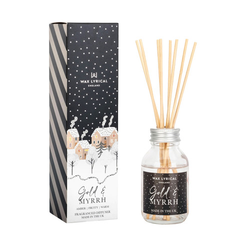 Gold & Myrrh reed diffuser with natural wooden reeds in a clear glass bottle, placed beside its black and white gift box decorated with a snowy village scene.