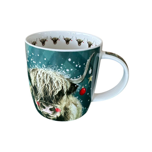 White mug featuring a festive Highland cow illustration on a teal background, with snowflakes and Christmas decorations hanging from its horns. The interior rim is decorated with a repeating Highland cow motif wearing red baubles.