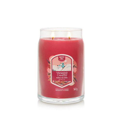 A red Yankee Candle in a glass jar with two wicks lit. The label reads “Santa on Skis” from the Après Ski Collection.