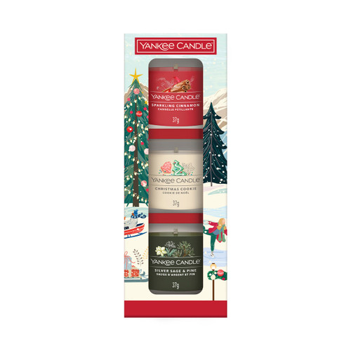 A Yankee Candle festive gift box containing three small candles in Sparkling Cinnamon, Christmas Cookie, and Silver Sage & Pine fragrances. The packaging is decorated with a snowy winter scene featuring a Christmas tree and people ice skating.