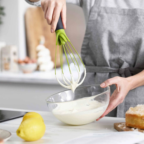 Person whisking cream in a glass bowl using a green and black Joseph Joseph Twist 2-in-1 silicone whisk.